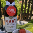 Load image into Gallery viewer, Pimms O'Clock Bottle Charm Gift Tag on a Pimm's bottle with fresh fruits in a garden setting.