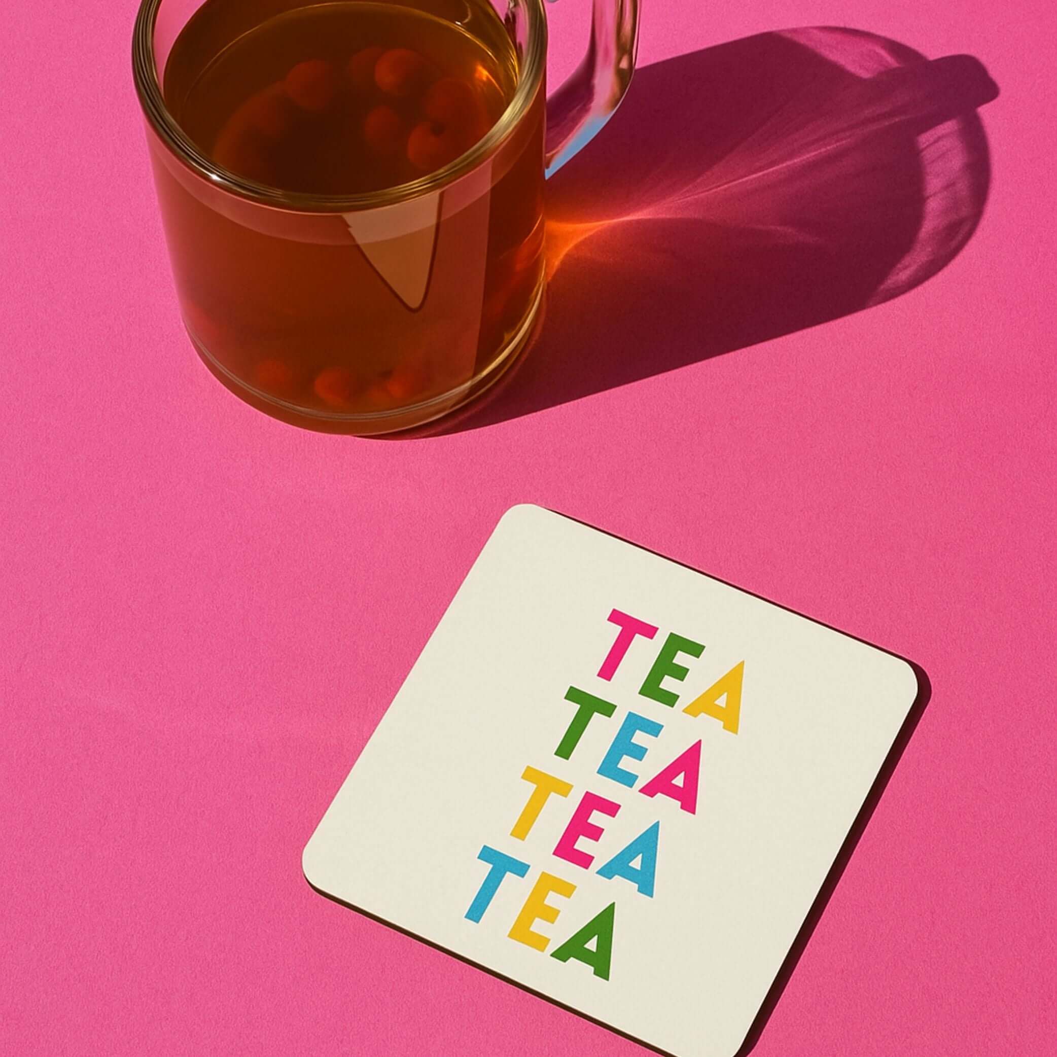Tea themed drink coaster with colorful 'TEA TEA TEA' text next to a glass of tea on a pink background.