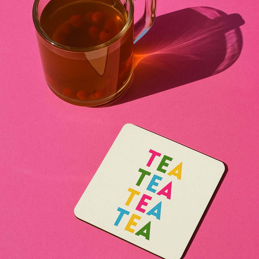 Tea themed drink coaster with colorful 'TEA TEA TEA' text next to a glass of tea on a pink background.
