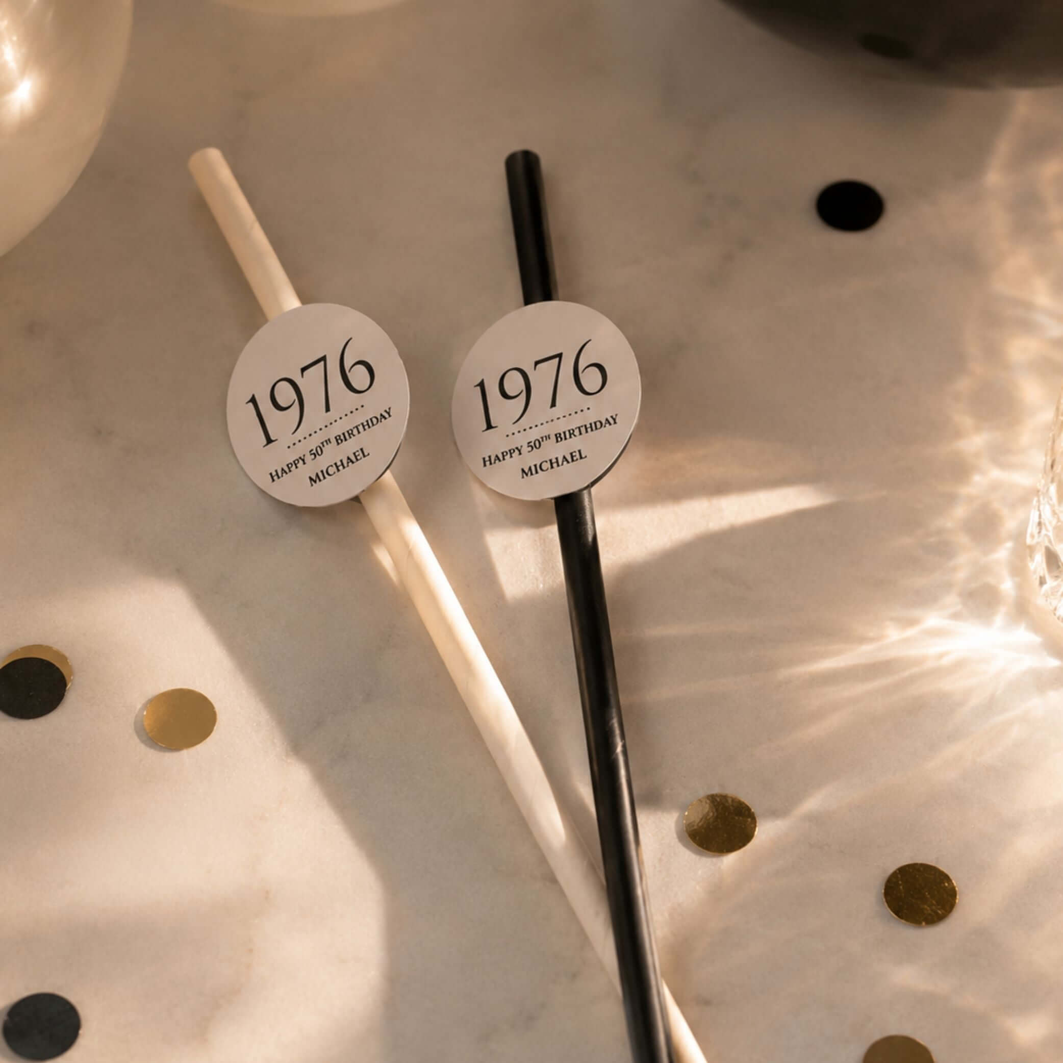 Personalised birthday year straw toppers with 1976 design on black and white straws, perfect for celebrations.