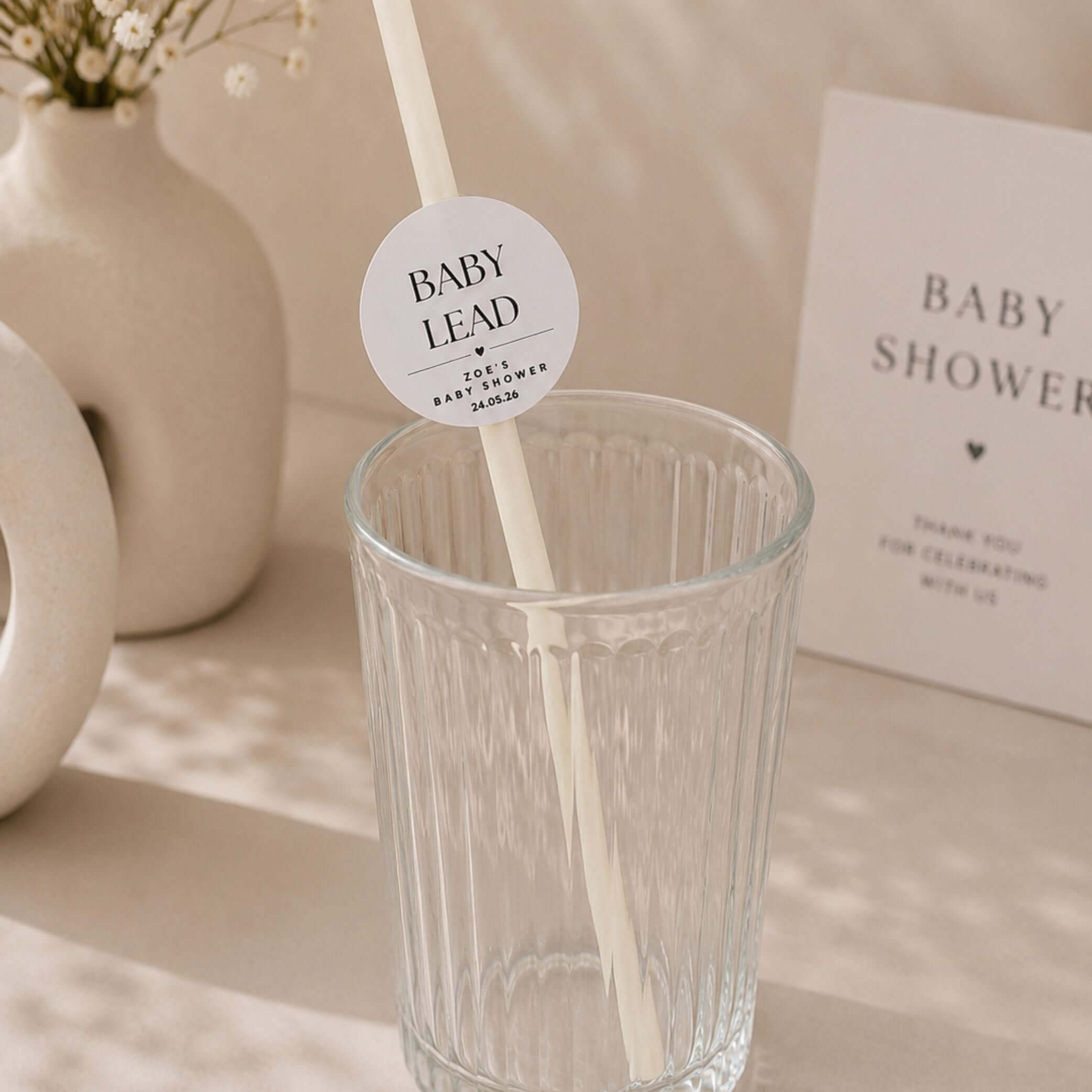 Personalised baby name paper straw toppers displayed in a glass at a baby shower event.