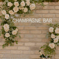 Load image into Gallery viewer, Champagne bar neon sign pre-order displayed among white roses at an elegant event.

