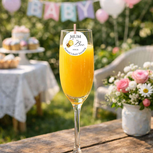 Mum To Bee edible drink topper on a glass of orange juice at a baby shower celebration.