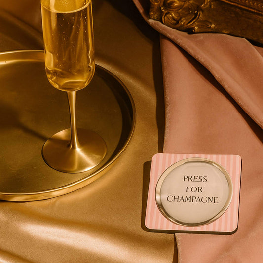 Press for champagne drink coaster beside a champagne flute on an elegant table setting.