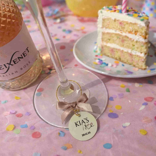 Personalised Birthday Party Wine Charms on a wine glass at a festive celebration with cake.