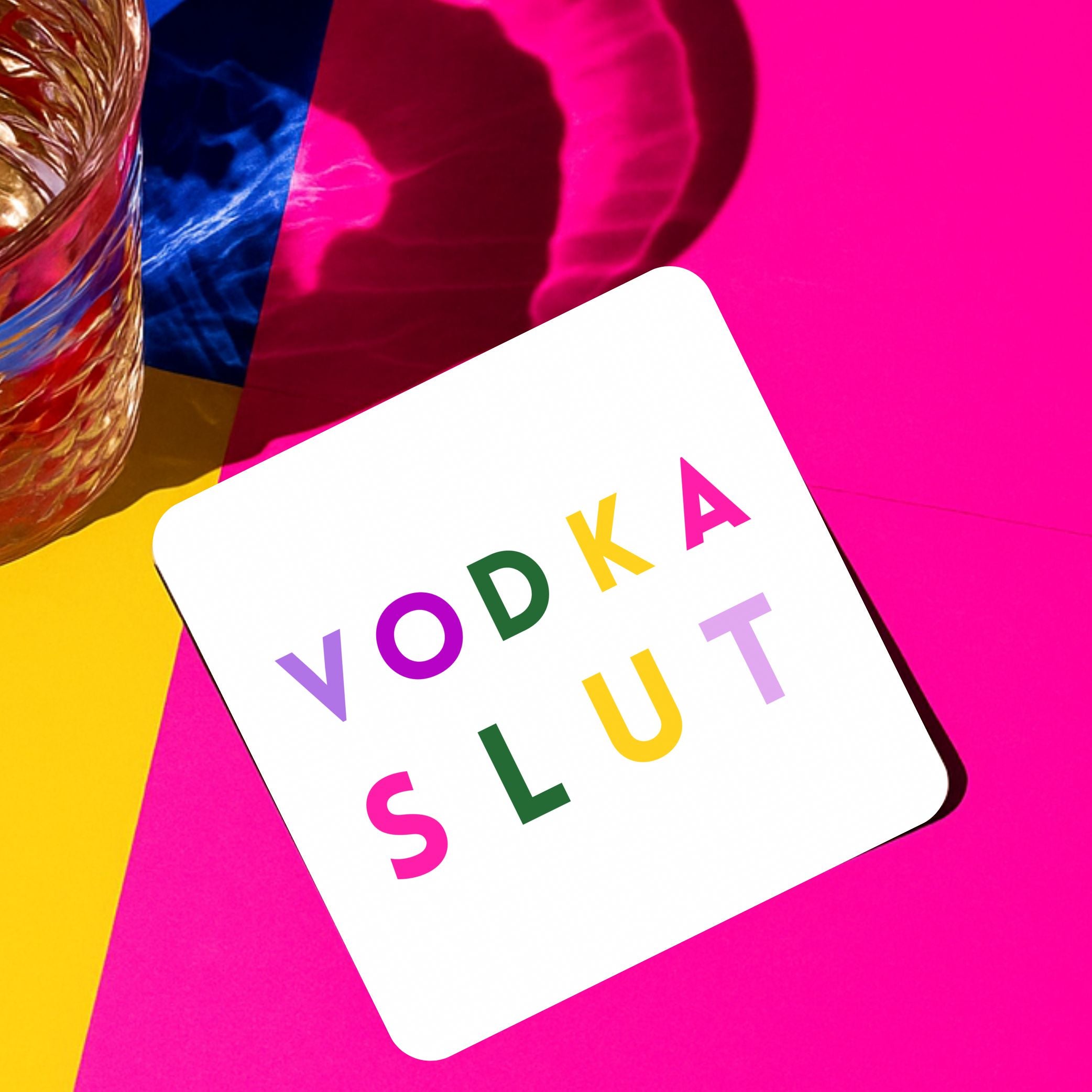 Colorful Vodka Slut Drink Coaster on a vibrant background next to a glass of drink.