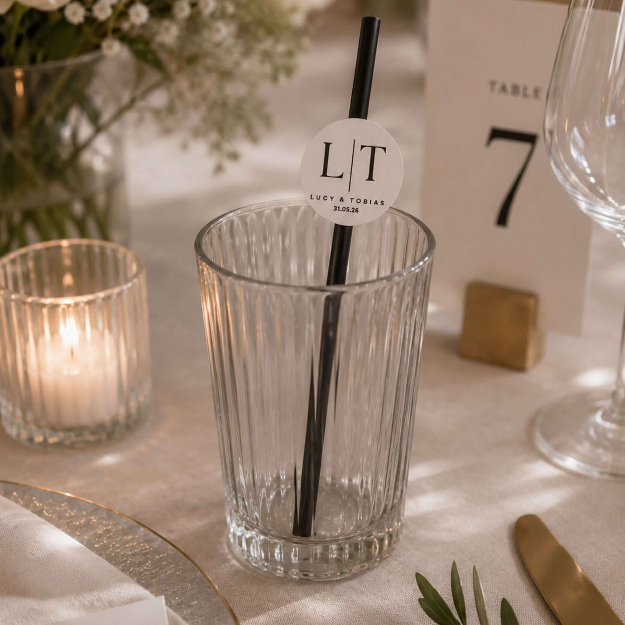 Occasion paper straws personalised initials toppers in a glass on elegantly decorated table with candlelight.
