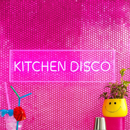 Kitchen Disco Neon Lightbox illuminating a vibrant pink backdrop with festive decor and beverages.