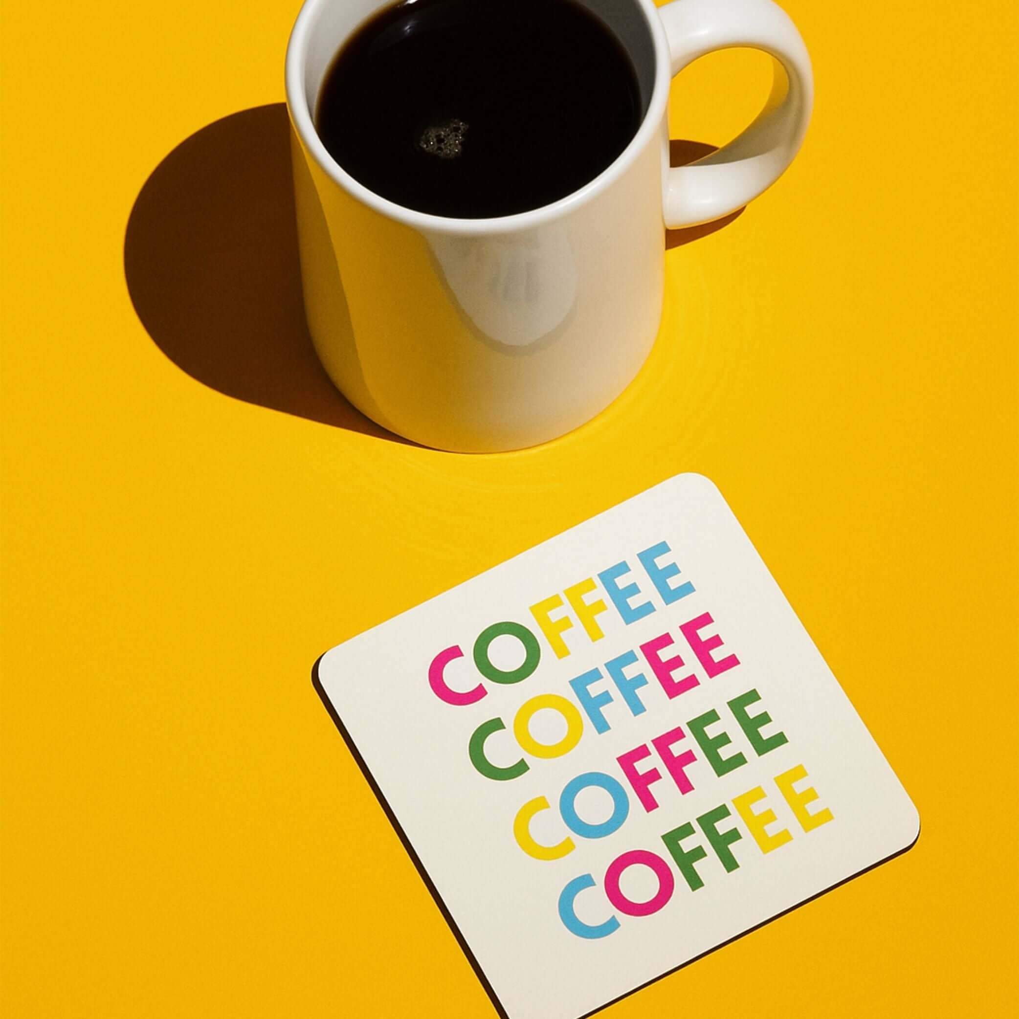 A coffee drink coaster with colorful 'COFFEE' text beside a cup of coffee on a bright yellow background.